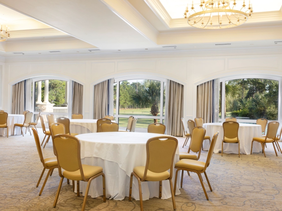 The Champions Ballroom at the Harbour Town Clubhouse set with three tables near three large windows arranged for a wedding. 