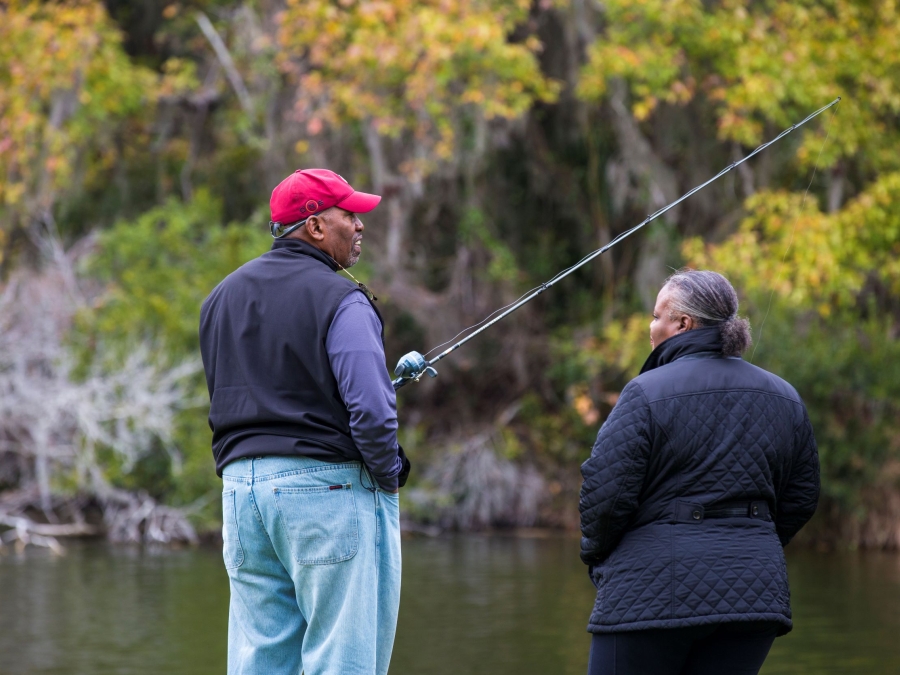 Couple standing by lake while the man is holding a fishing pole.